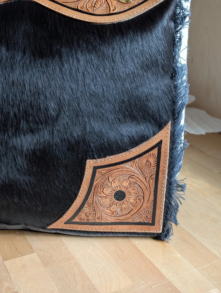 Black cowhide throw pillow with tan leather floral embroidery and frayed edges complements the cartwright hand-tooled bag