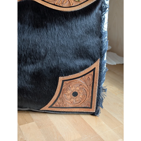 Black cowhide throw pillow with tan leather floral embroidery and frayed edges complements the cartwright hand-tooled bag