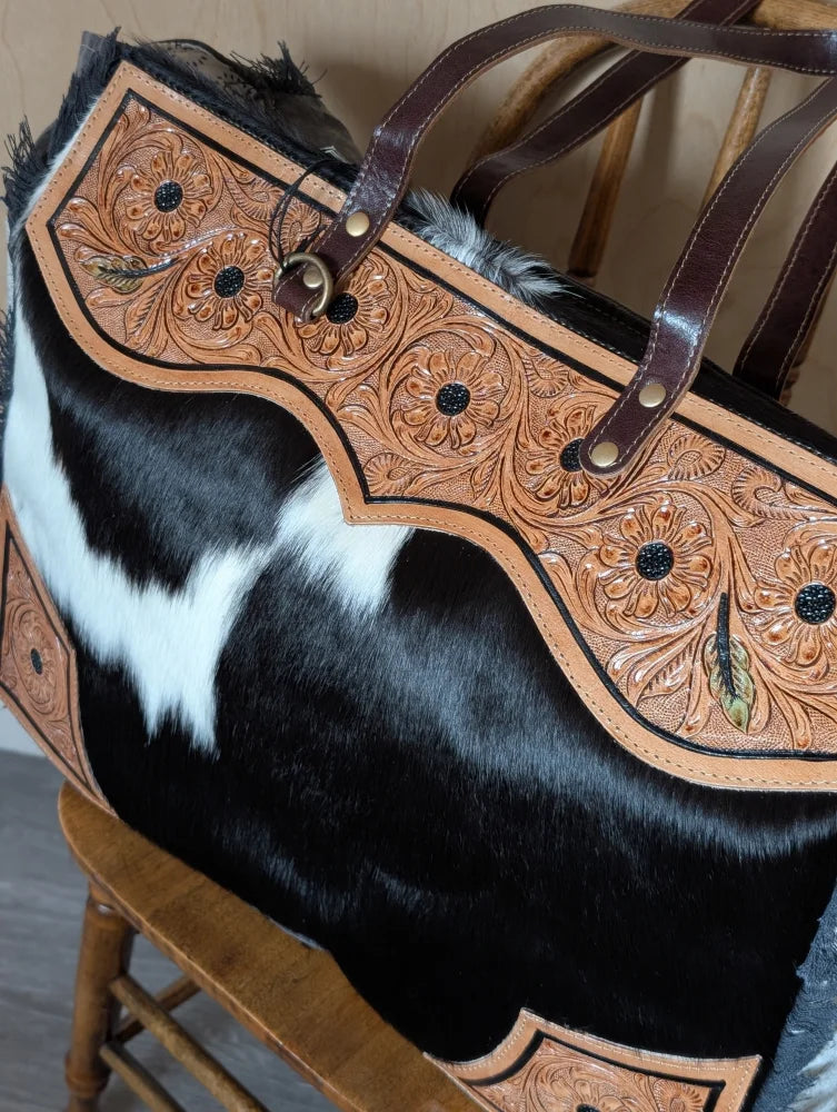 The sunflower weekender bag is a cartwright hand-tooled bag with floral leather, black studs, zippered pocket, and hair-on hide body