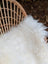 A plush natural white icelandic sheepskin throw with long wool draped over a woven wicker chair