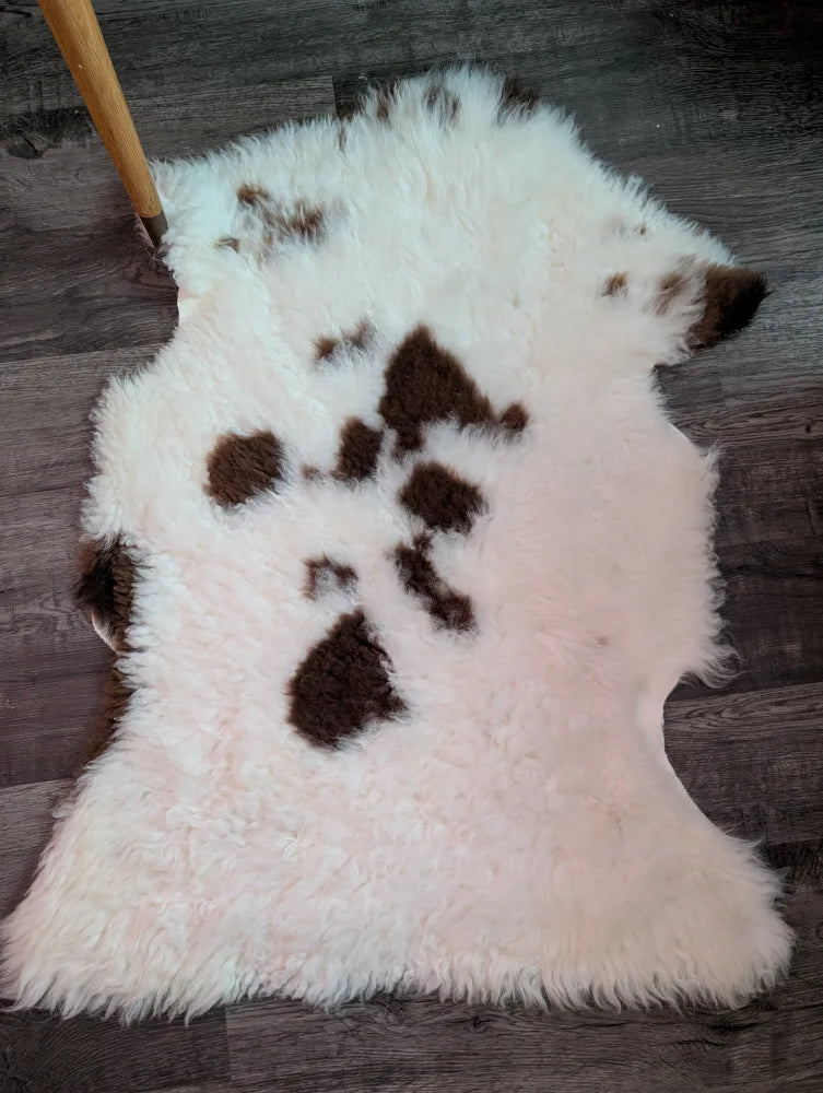A fluffy white and brown tibet highland spotted grade a- sheepskin rug with a natural irregular shape
