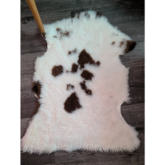 A fluffy white and brown tibet highland spotted grade a- sheepskin rug with a natural irregular shape