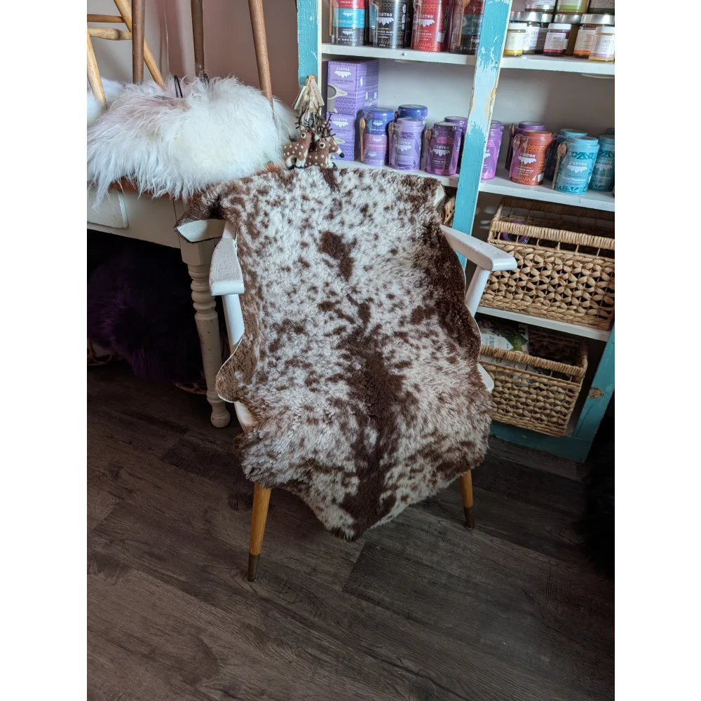 Brown and white highland spotted grade b sheepskin rug draped over wooden chair perfect for cozy decor