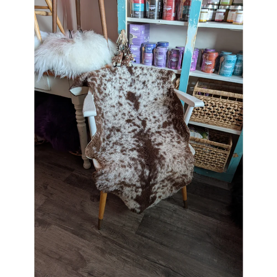 Brown and white highland spotted grade b sheepskin rug draped over wooden chair perfect for cozy decor