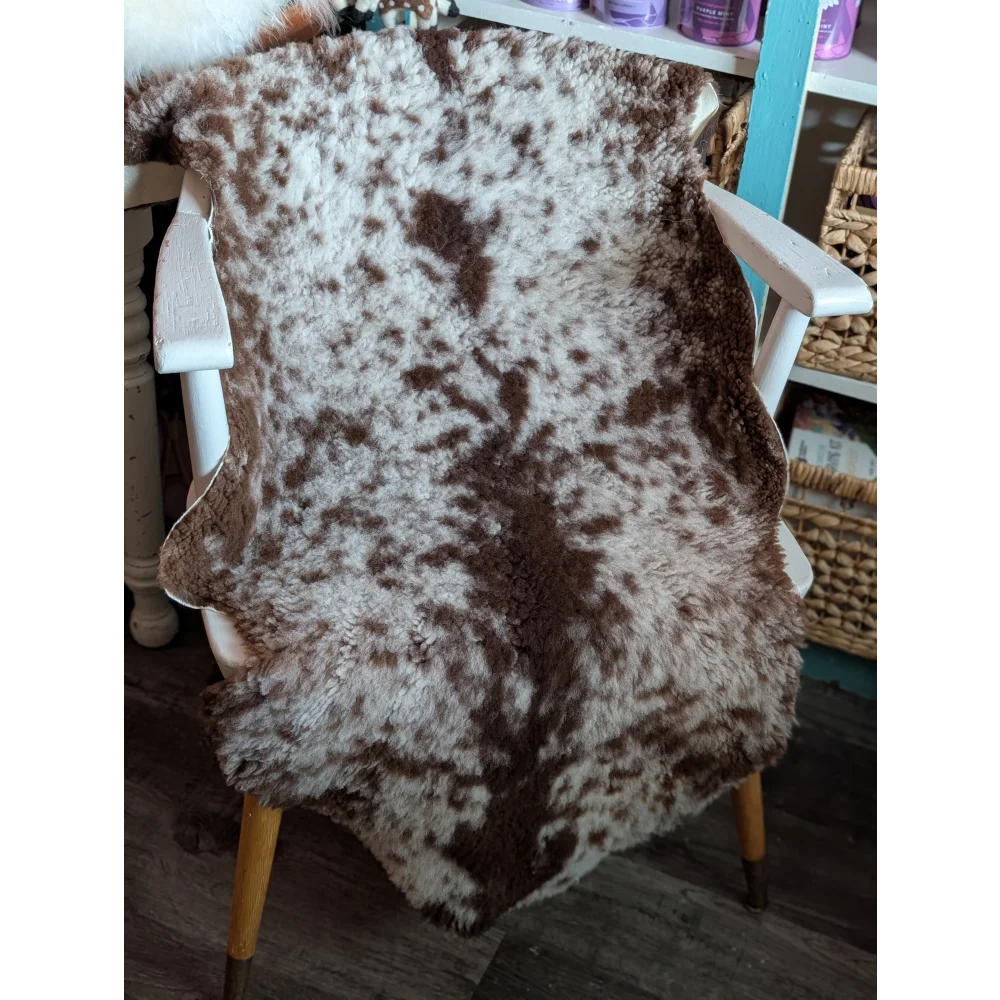 A plush irregular brown and white highland spotted grade b sheepskin rug draped over a wooden chair