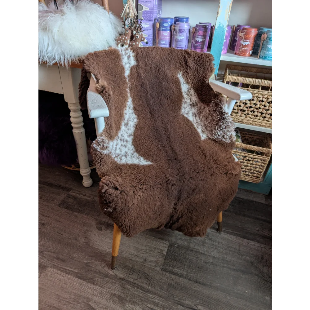 Brown highland spotted grade b sheepskin chair cover with white markings draped on wooden armchair