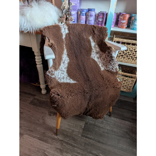 Brown highland spotted grade b sheepskin chair cover with white markings draped on wooden armchair