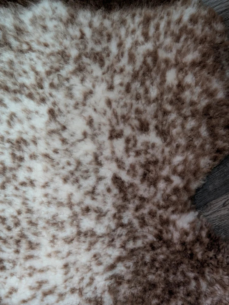 A plush cream and brown speckled faux fur throw blanket with soft texture made from grade a- tibet highland spotted sheepskins