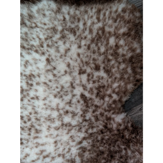 A plush cream and brown speckled faux fur throw blanket with soft texture made from grade a- tibet highland spotted sheepskins