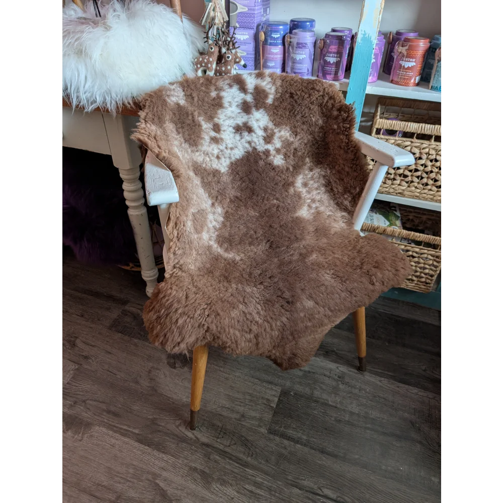 A cozy brown and white tibet highland spotted grade a- sheepskin chair cover on a wooden armchair