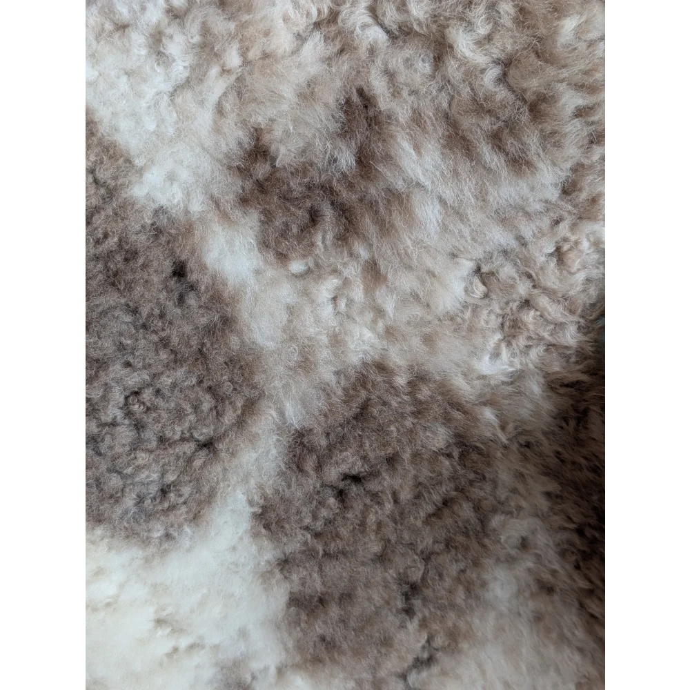 A plush tibet highland spotted grade a- sheepskin rug in natural cream and light brown tones with curly texture