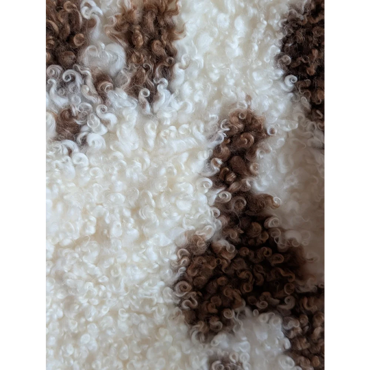 A plush white tibet highland spotted grade a- sheepskin with curly texture and irregular brown patches
