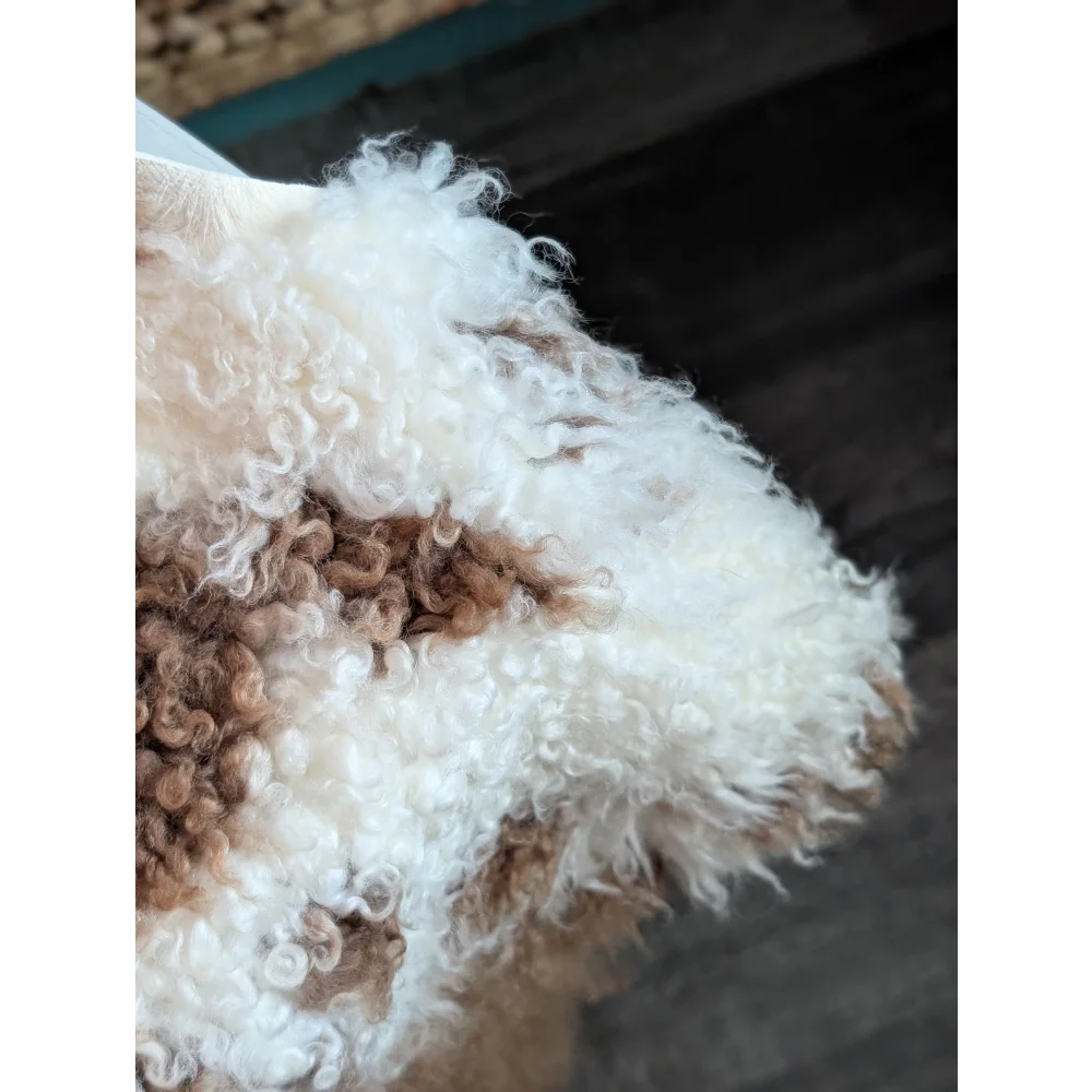 A fluffy white and brown tibet highland spotted dog on a soft grade a- sheepskin with curly textured coat