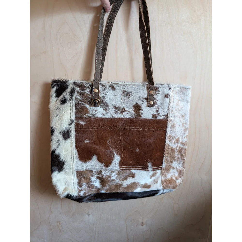 Brown and white real cowhide patchwork tote bag with leather straps featuring a front pocket from cowhide rugs collection