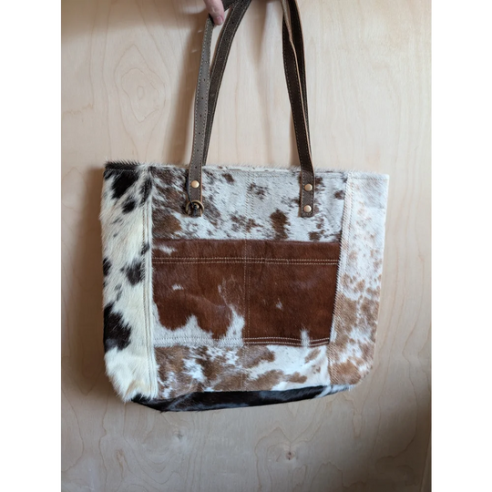 Brown and white real cowhide patchwork tote bag with leather straps featuring a front pocket from cowhide rugs collection
