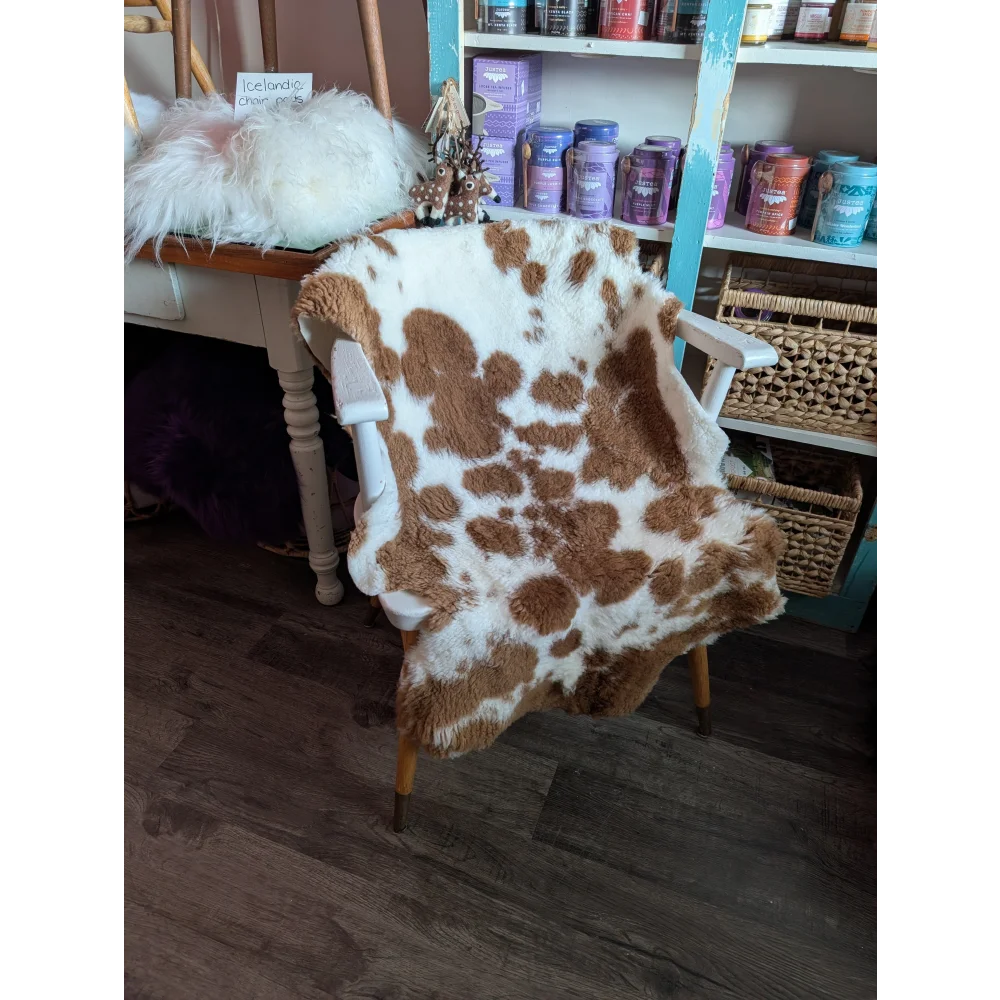 A cozy brown and white highland spotted grade b sheepskin rug draped over a wooden chair