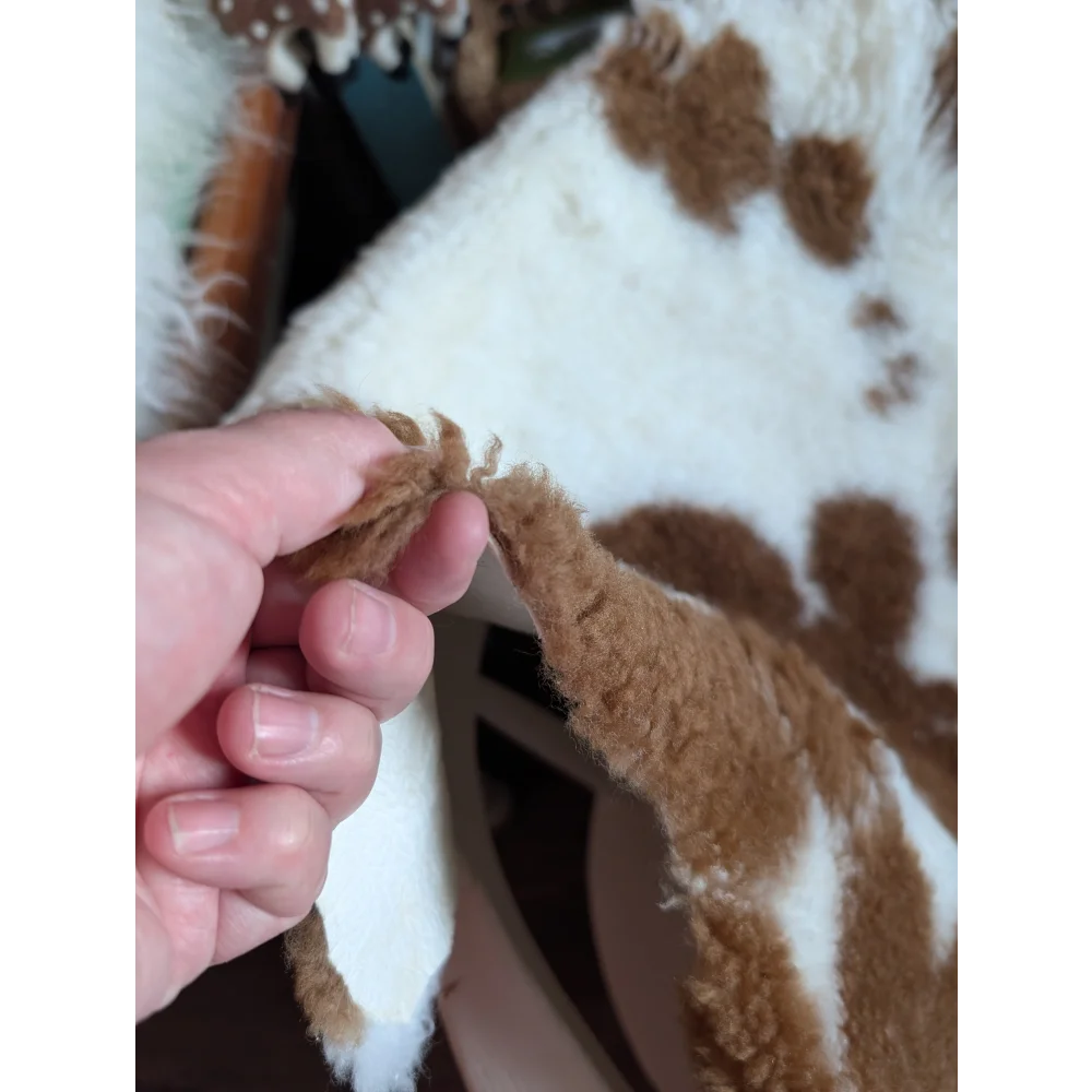 A plush white and brown highland spotted grade b sheepskin rug with a soft fuzzy texture