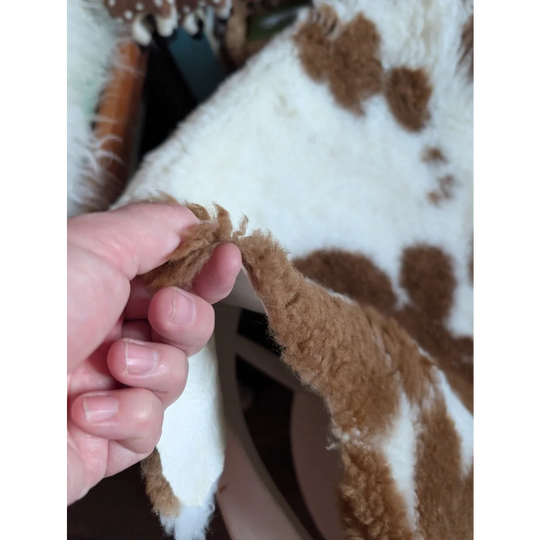 A plush white and brown highland spotted grade b sheepskin rug with a soft fuzzy texture