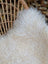 A plush natural white icelandic sheepskin throw with long wool fibers draped over a woven wicker chair