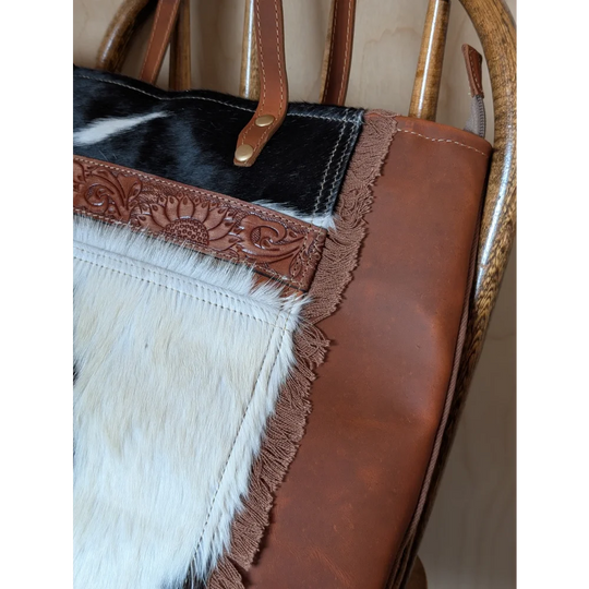 A stylish oakley bag featuring a real cowhide black and white patch with brown leather floral trim and frayed edges spacious bag