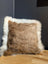 A square plush cushion in natural brown cowhide with soft white merino sheepskin trim for cozy decor