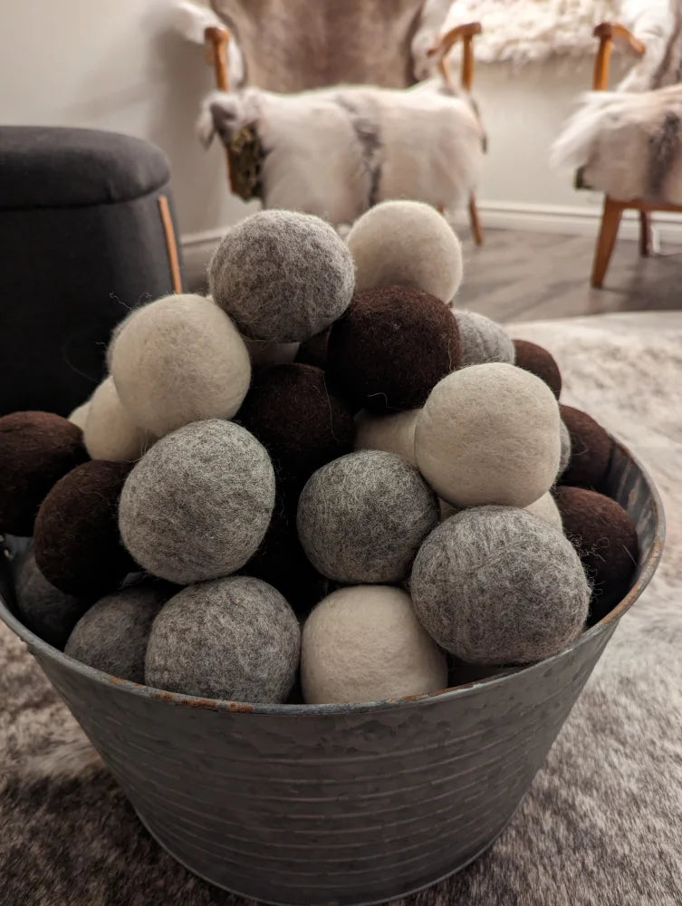 A rustic metal bucket filled with gray and cream moss creek wool dryer balls made from pure merino wool