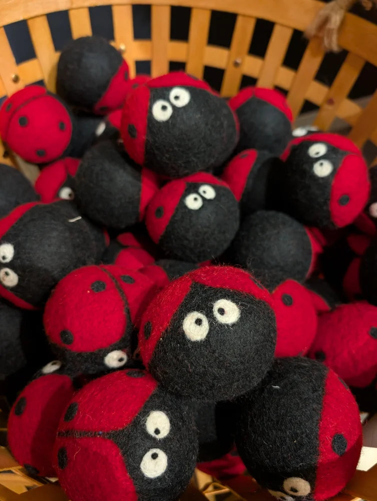 Red and black felt ladybug dryer balls with googly eyes in a woven basket