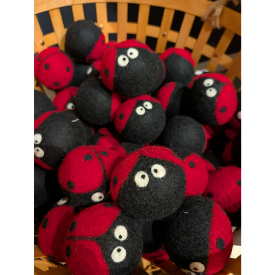 Red and black felt ladybug dryer balls with googly eyes in a woven basket