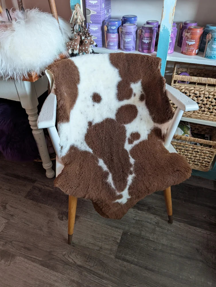Brown and white highland spotted grade b sheepskin fur throw draped over a white wooden chair
