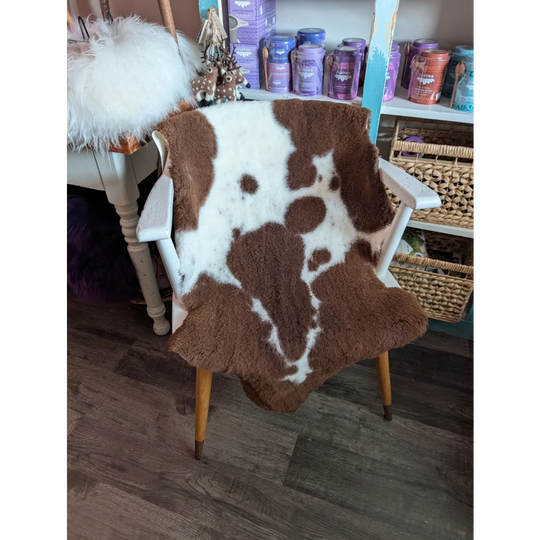 Brown and white highland spotted grade b sheepskin fur throw draped over a white wooden chair