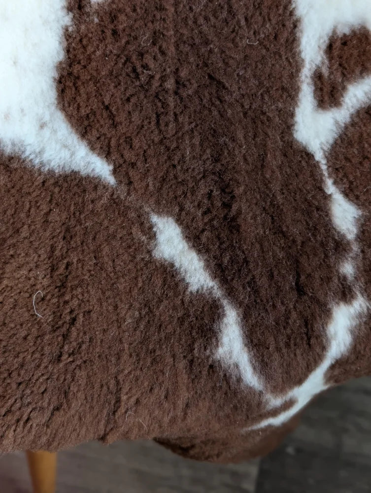 A plush brown and white highland spotted grade b sheepskin blanket with a soft fuzzy texture perfect for cozy use