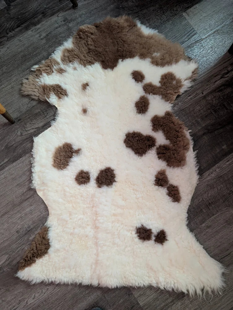 A plush cream-colored tibet highland spotted grade a- sheepskin rug with soft fluffy texture and brown patches