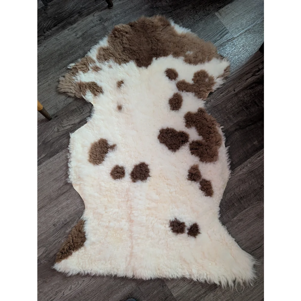 A plush cream-colored tibet highland spotted grade a- sheepskin rug with soft fluffy texture and brown patches