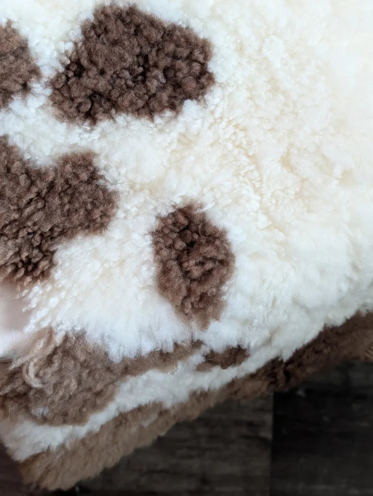 A plush cream-colored tibet highland spotted blanket with soft brown cow-print patches made from grade a- sheepskins