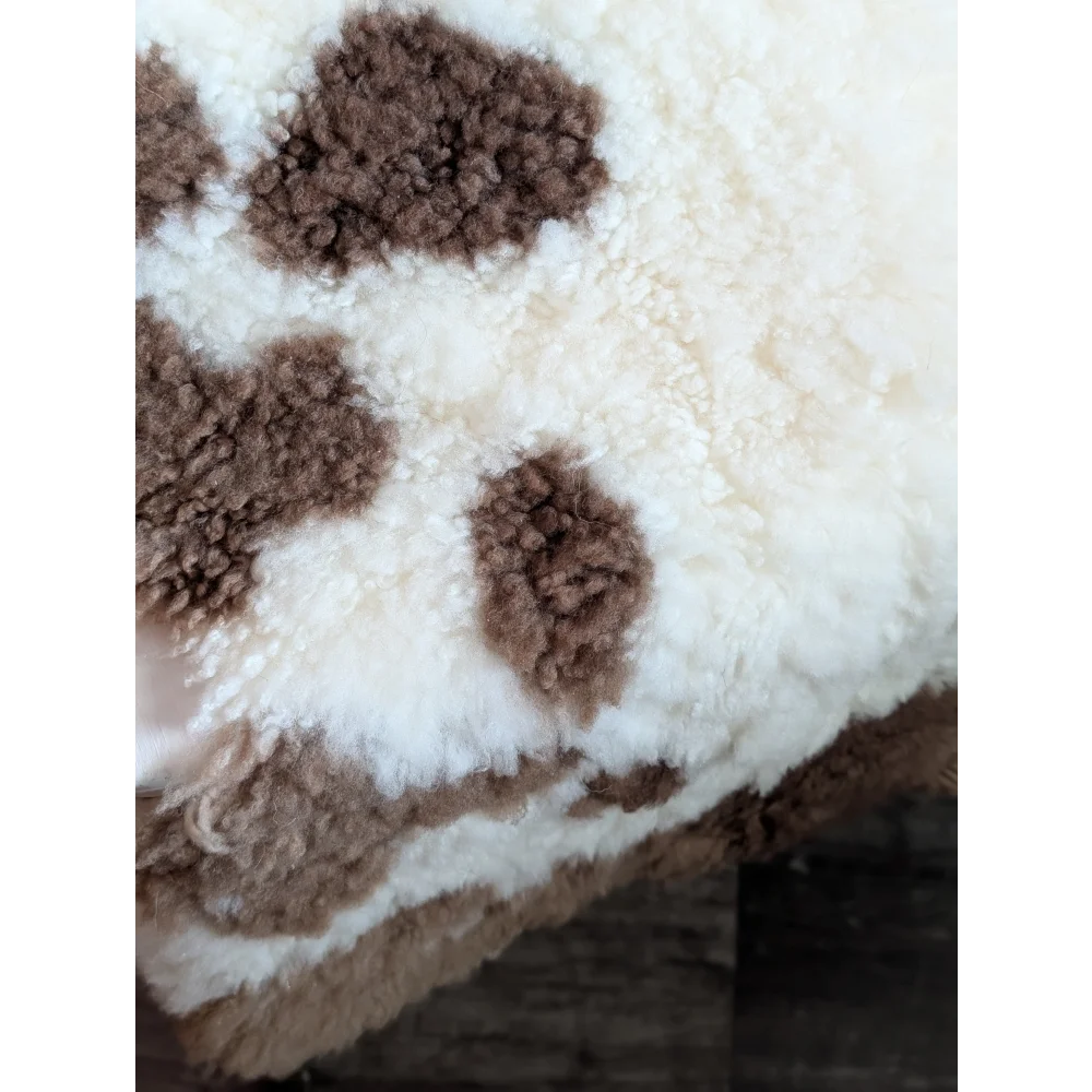 A plush cream-colored tibet highland spotted blanket with soft brown cow-print patches made from grade a- sheepskins