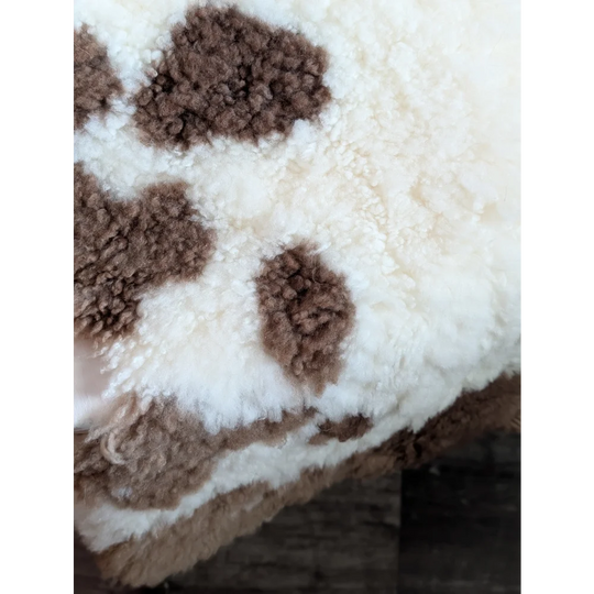 A plush cream-colored tibet highland spotted blanket with soft brown cow-print patches made from grade a- sheepskins