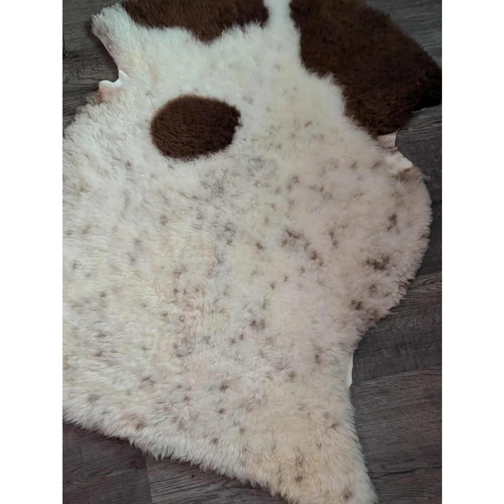 A cream-colored tibet highland spotted grade a- sheepskin rug with brown speckles and dark patches resembling ears