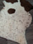 A cream-colored tibet highland spotted grade a- sheepskin rug with brown speckles and dark patches resembling ears