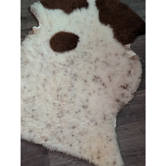 A cream-colored tibet highland spotted grade a- sheepskin rug with brown speckles and dark patches resembling ears