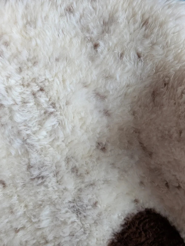 A plush off-white tibet highland spotted grade a- sheepskin rug with soft curly fibers and subtle brown speckles