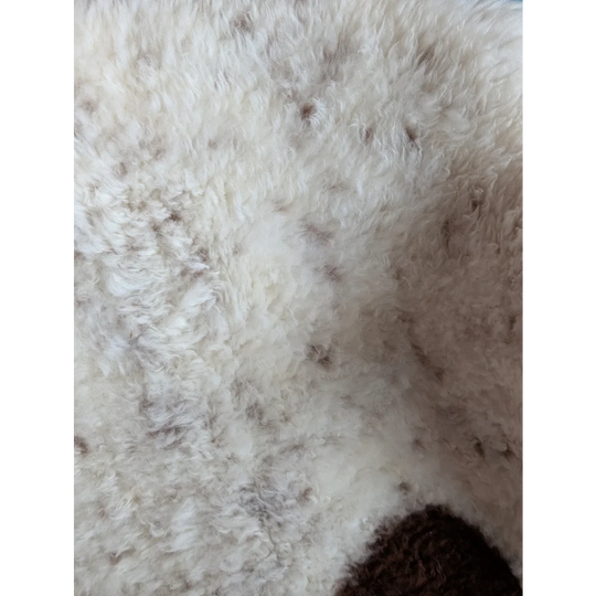 A plush off-white tibet highland spotted grade a- sheepskin rug with soft curly fibers and subtle brown speckles