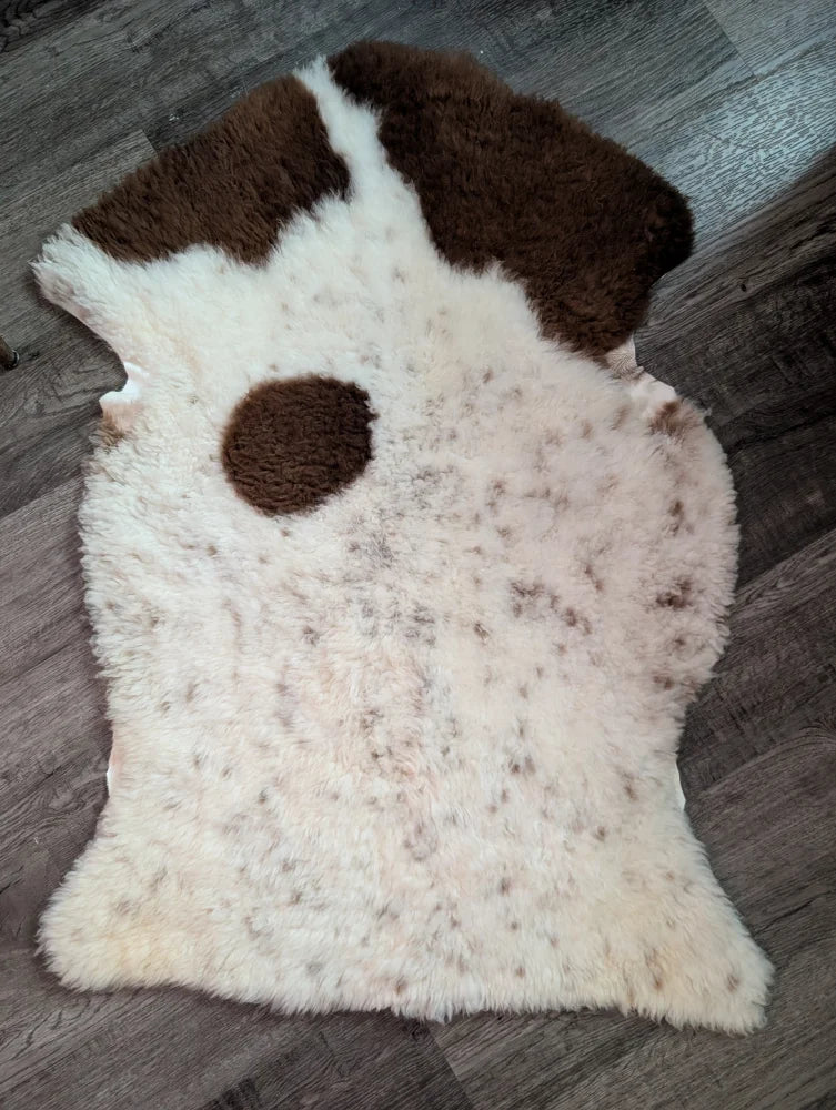 A plush cream-colored tibet highland spotted grade a- sheepskin rug with irregular brown patches and fluffy texture