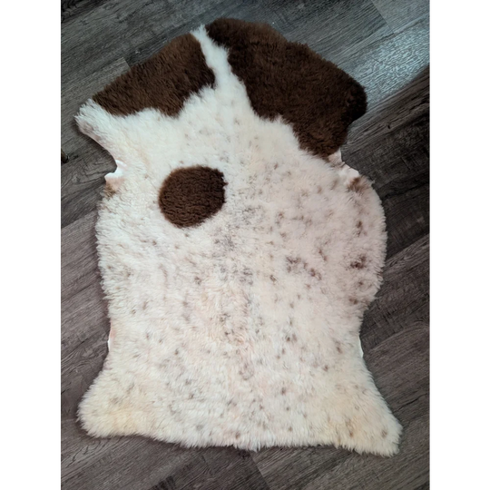 A plush cream-colored tibet highland spotted grade a- sheepskin rug with irregular brown patches and fluffy texture