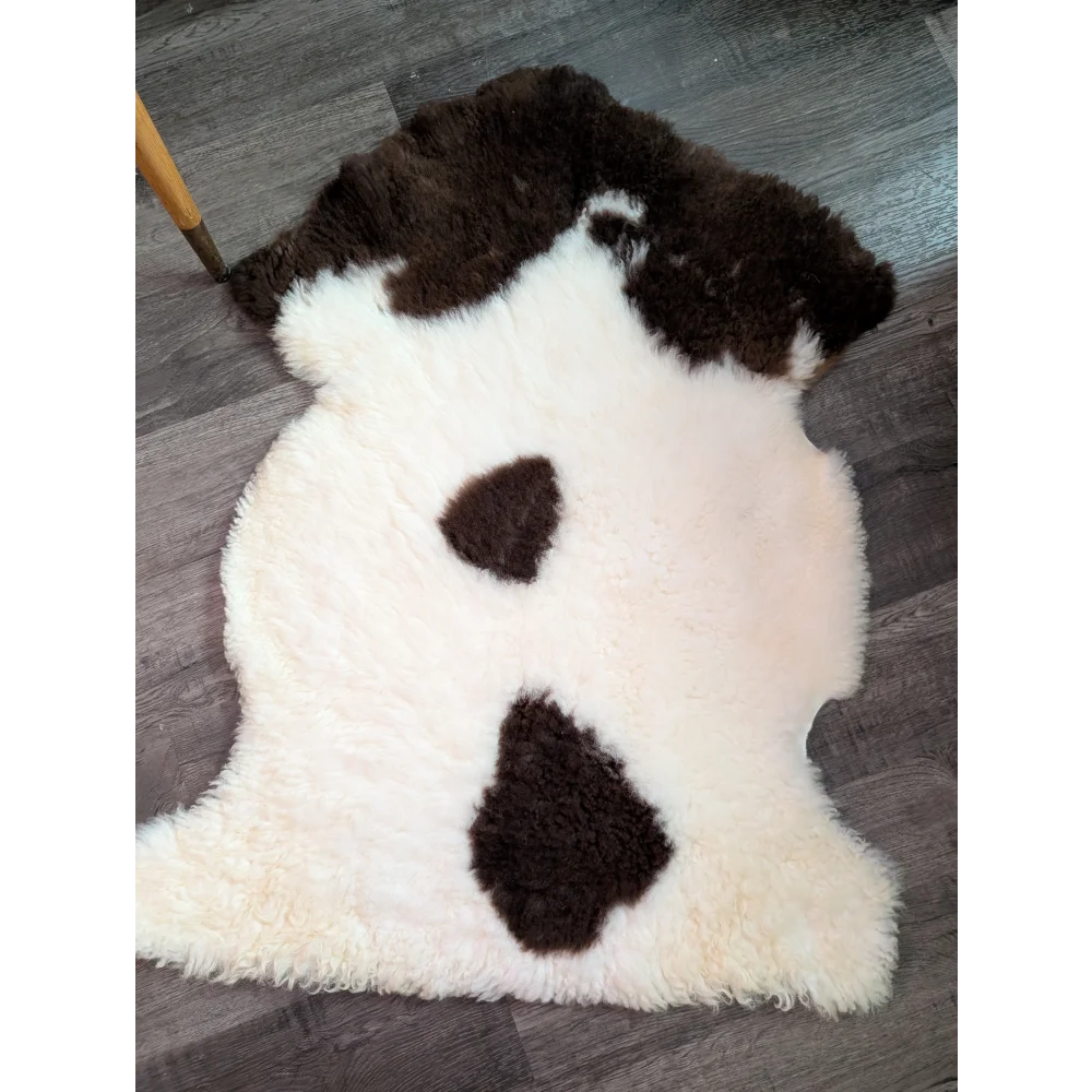 A plush cream-colored tibet highland spotted grade a- sheepskin rug with dark brown patches shaped like a cow face