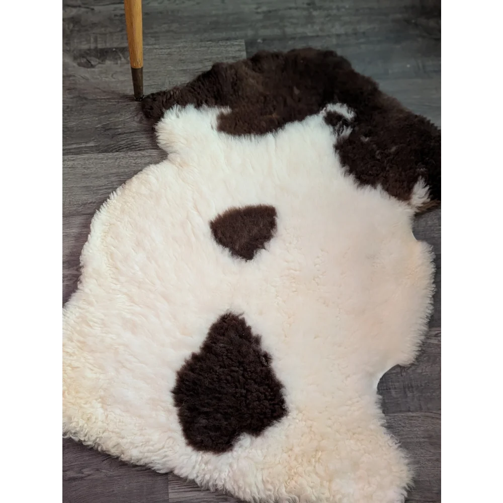 A plush cream-colored tibet highland spotted grade a- sheepskin rug with dark brown patches shaped like a dog face
