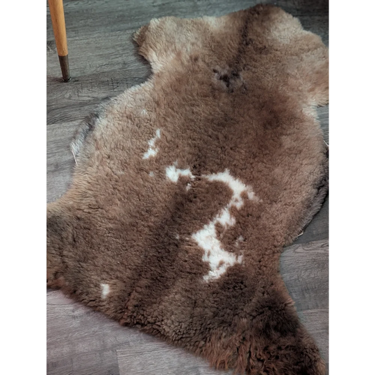 A soft natural brown tibet highland spotted grade a- sheepskin rug with fluffy texture and white patches