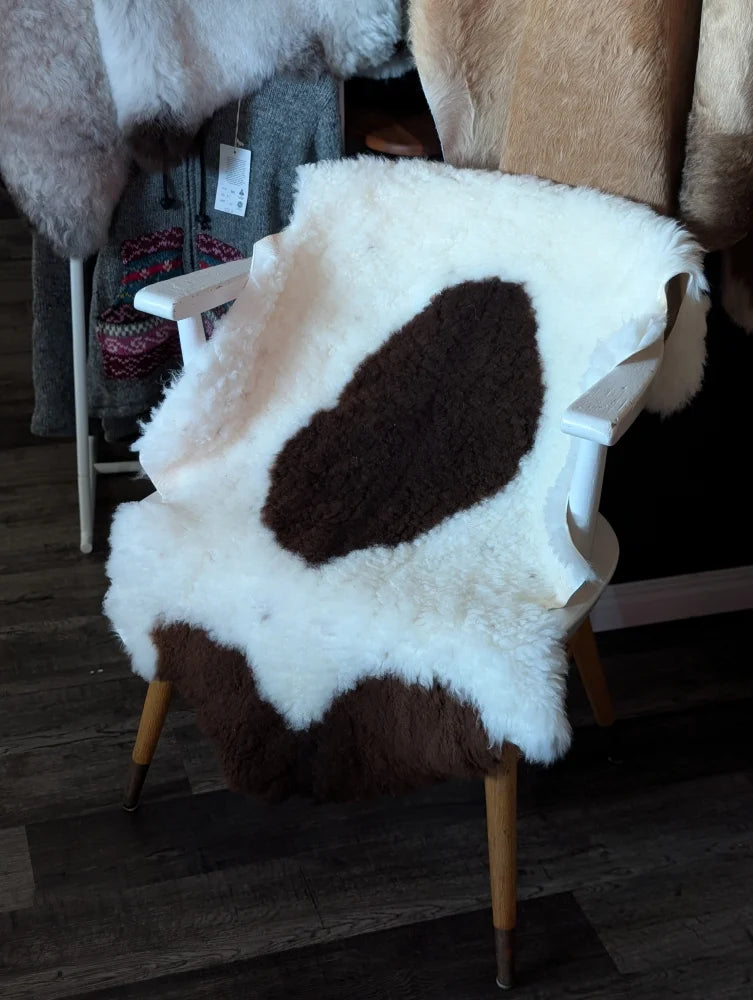White and brown tibet highland spotted grade a- sheepskin rug draped over white wooden chair by nat’s grade