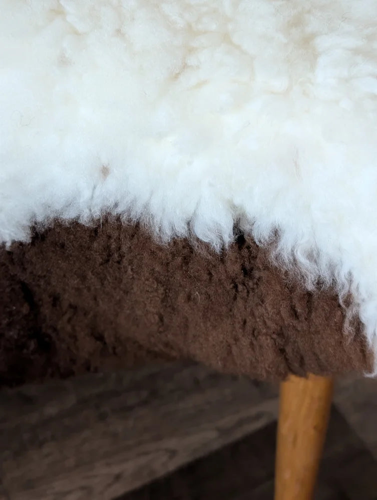 A plush white and brown tibet highland spotted grade a- sheepskin stool with wooden legs from nat’s grade collection