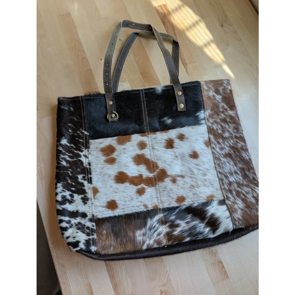 A patchwork cowhide tote bag with black white and brown panels and dark leather handles made from real cowhide
