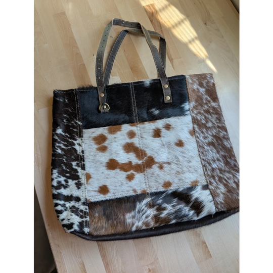 A patchwork cowhide tote bag with black white and brown panels and dark leather handles made from real cowhide